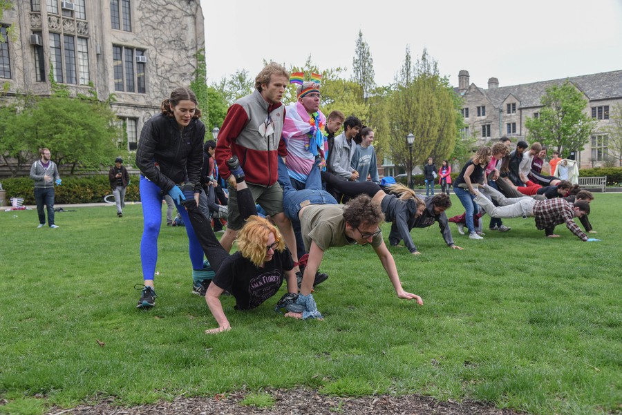 Many people on the Quad of UChicago in teams of five. On each team, three people hold the legs of two people in a wheelbarrow position. Front and center is a team made up of L. A. Lanquist and a group named Cactus Emoji.